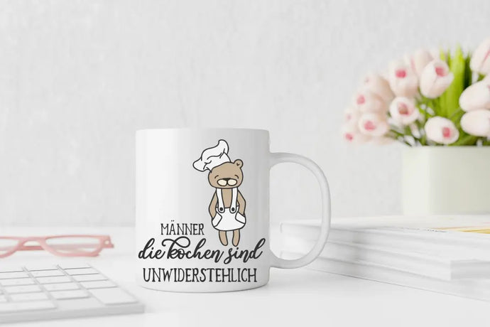 Bild der Koch-Bären-Tasse mit dem humorvollen Schriftzug 'Männer die kochen, sind unwiderstehlich' und einem Bären in Kochmütze